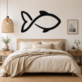 Black metal fish wall art with a simple silhouette design, mounted on a wall above a bed in a neutral bedroom.