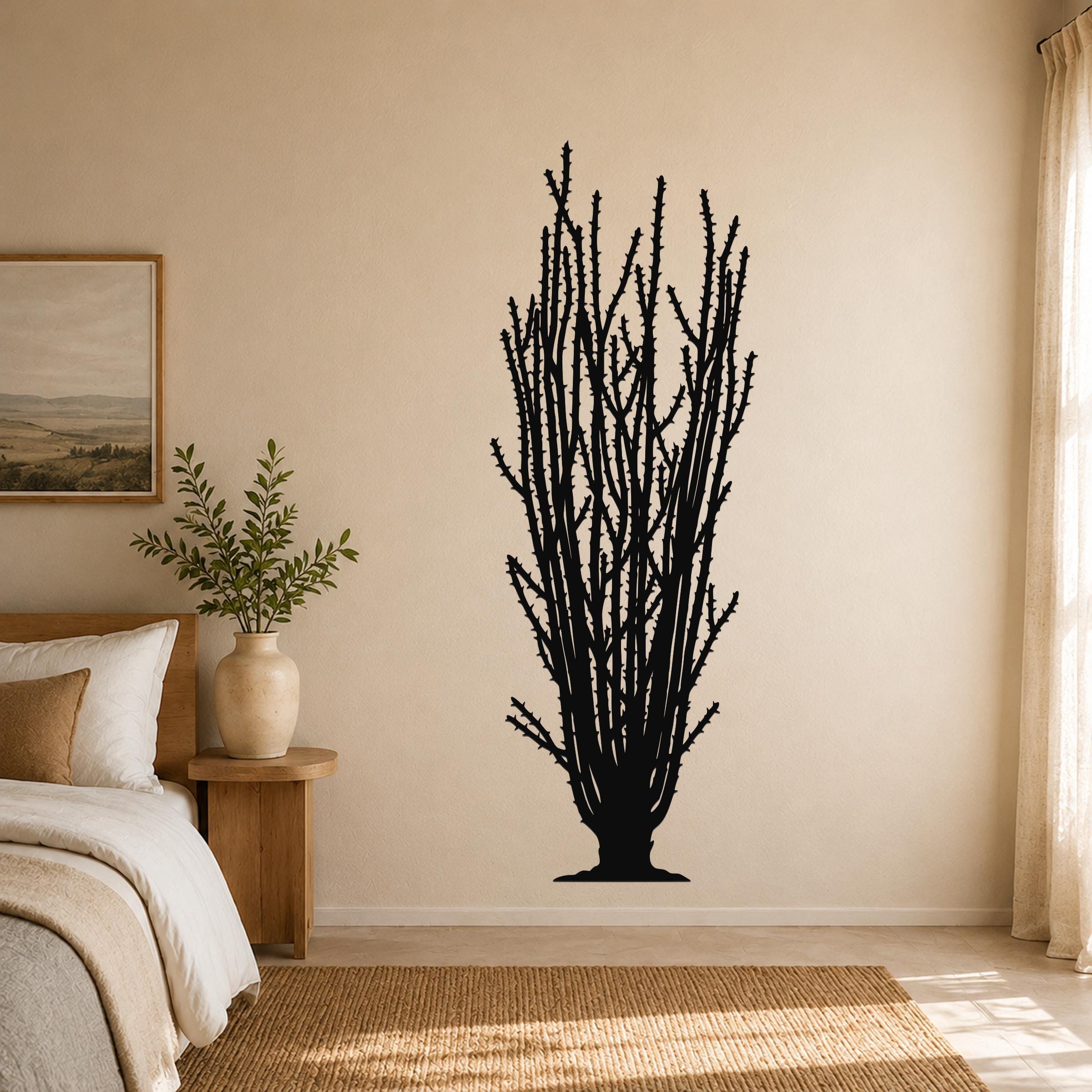 Black metal ocotillo wall art with spiny branch cutouts, mounted on a beige bedroom wall above a woven rug.