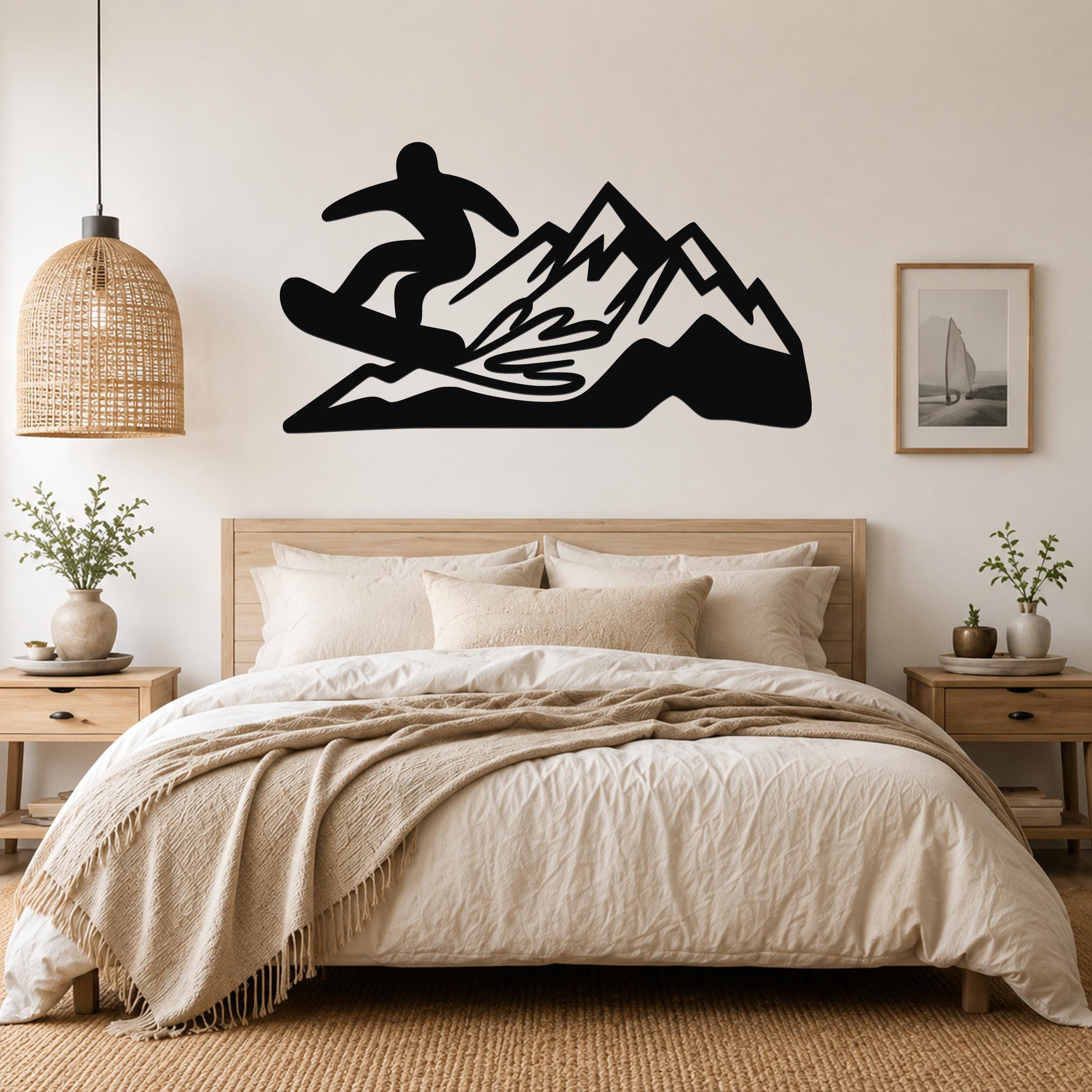 Black metal wall art featuring a snowboarder silhouette above a mountain range, mounted on a bedroom wall above a wooden bed.
