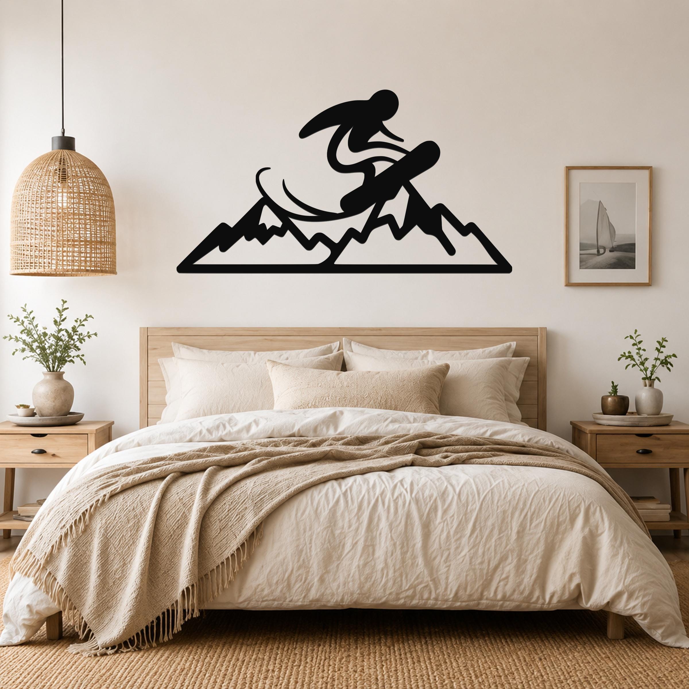 Black metal wall art featuring a snowboarder silhouette above a mountain range, mounted above a bed in a bedroom.