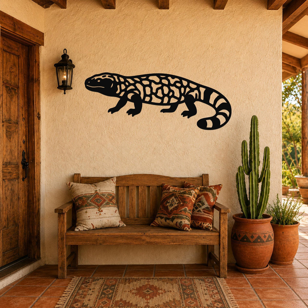 Black metal Gila monster wall art with intricate internal cutouts, mounted on a stucco wall above a wooden bench in a rustic patio setting.