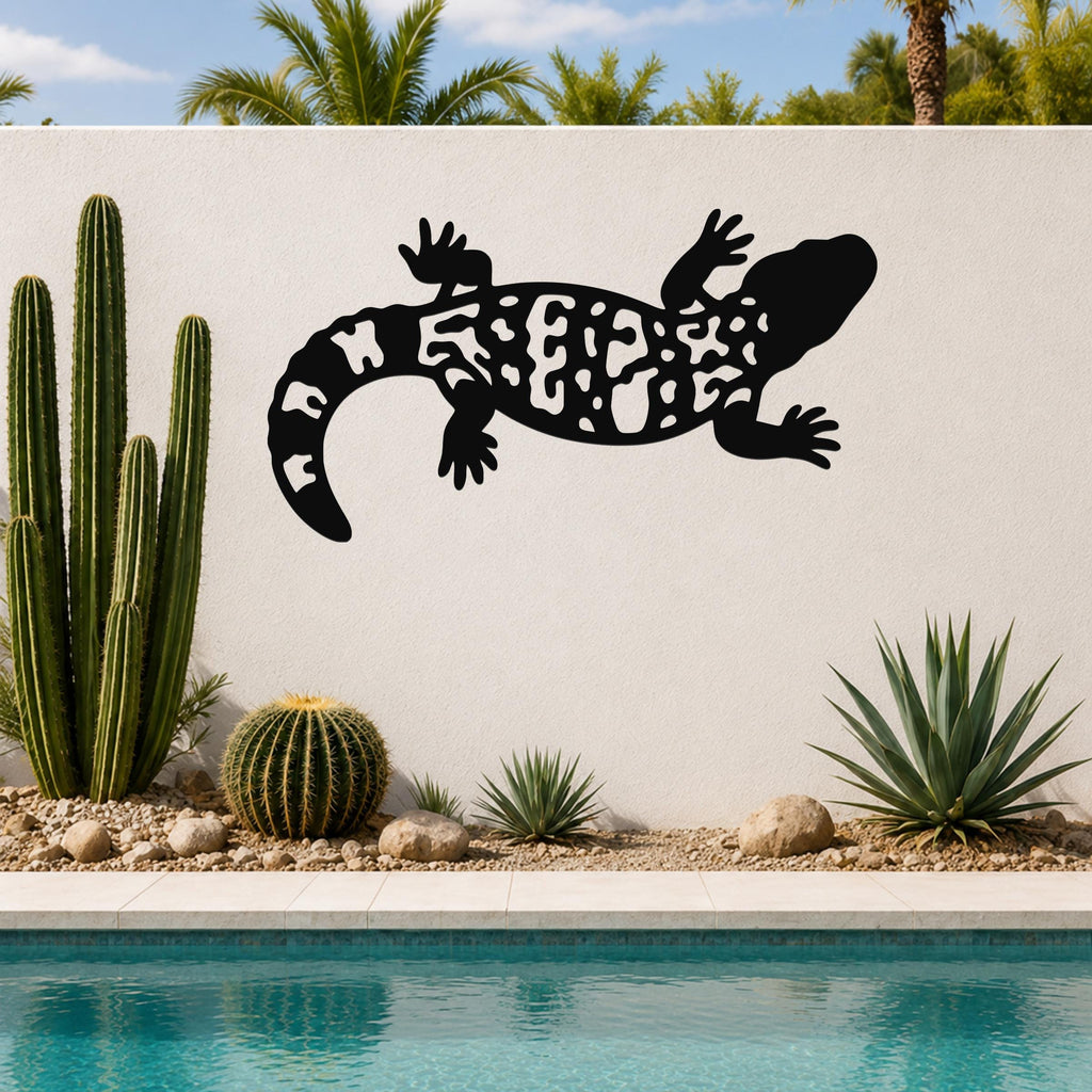 Black metal Gila monster wall art with intricate cutout patterns, mounted on a white outdoor wall beside a pool and desert plants.