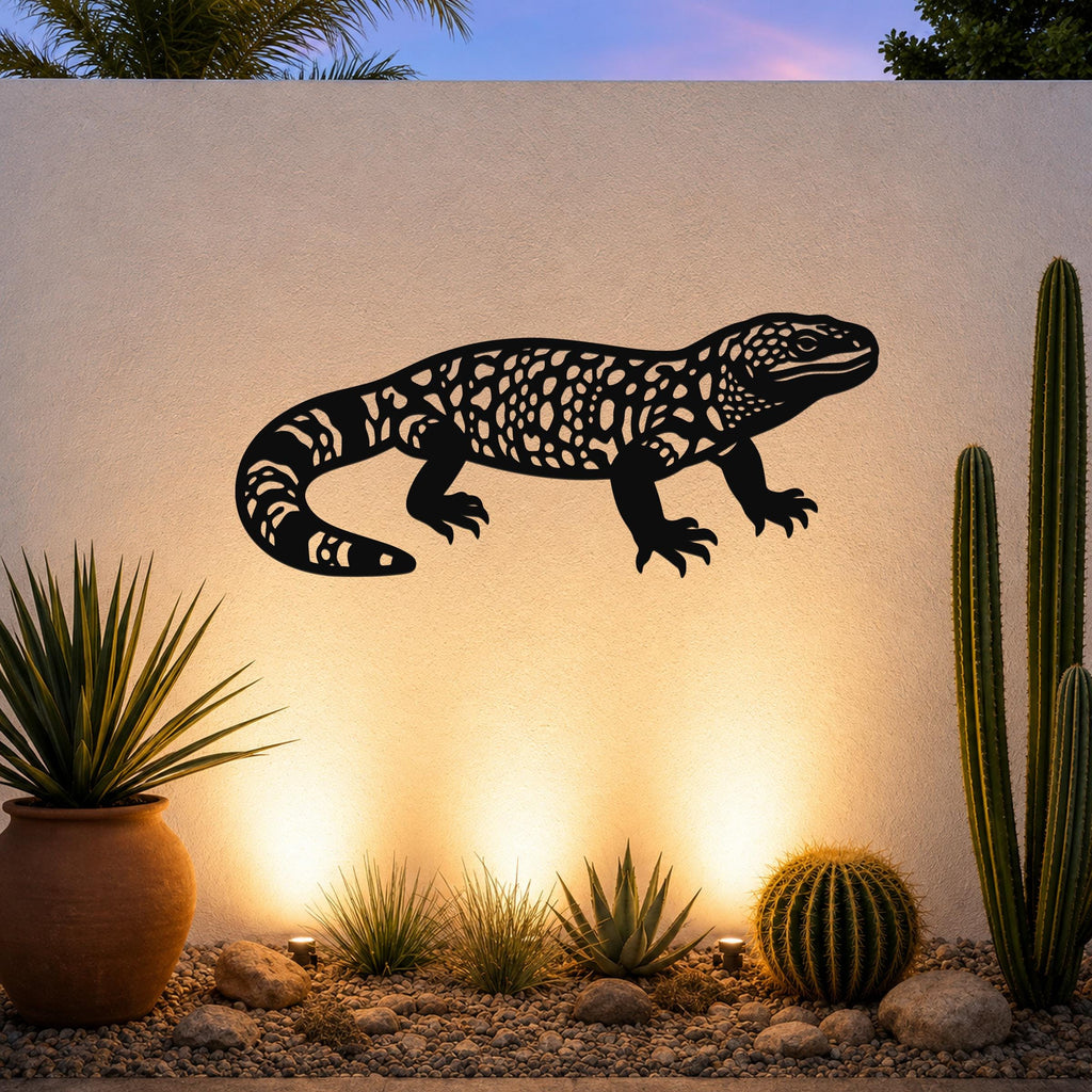 Black metal wall art of a Gila monster with intricate cutout patterns, mounted on a textured outdoor wall above a desert garden with cacti and warm uplighting.