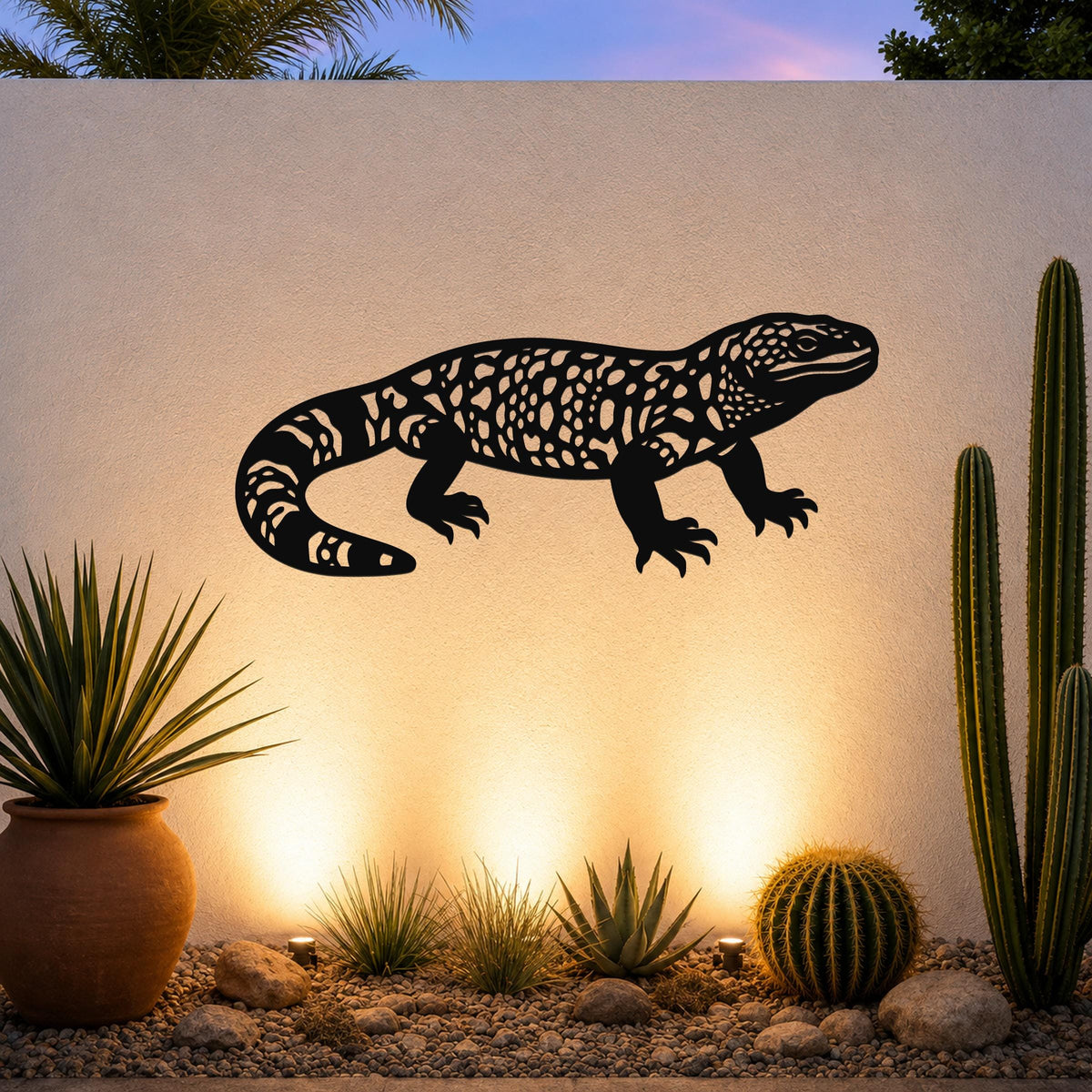Black metal wall art of a Gila monster with intricate cutout patterns, mounted on a textured outdoor wall above a desert garden with cacti and warm uplighting.