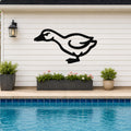 Black metal goose wall art silhouette mounted on a white horizontal siding wall above a pool, with a black lantern and potted plants nearby.