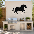 Black metal horse silhouette wall art mounted on a light-colored outdoor wall above a built-in grill and counter.
