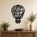 Black metal wall art cutout of a hot air balloon with intricate swirl and line patterns, mounted on a wall above a wooden console table with potted plants.