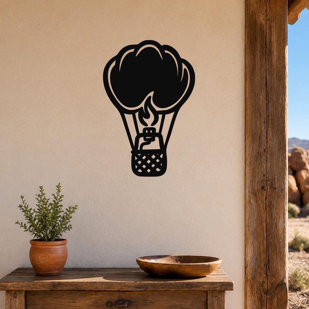 Black metal hot air balloon wall art with flame and basket cutouts, mounted on a beige wall above a wooden table in a rustic outdoor entryway.