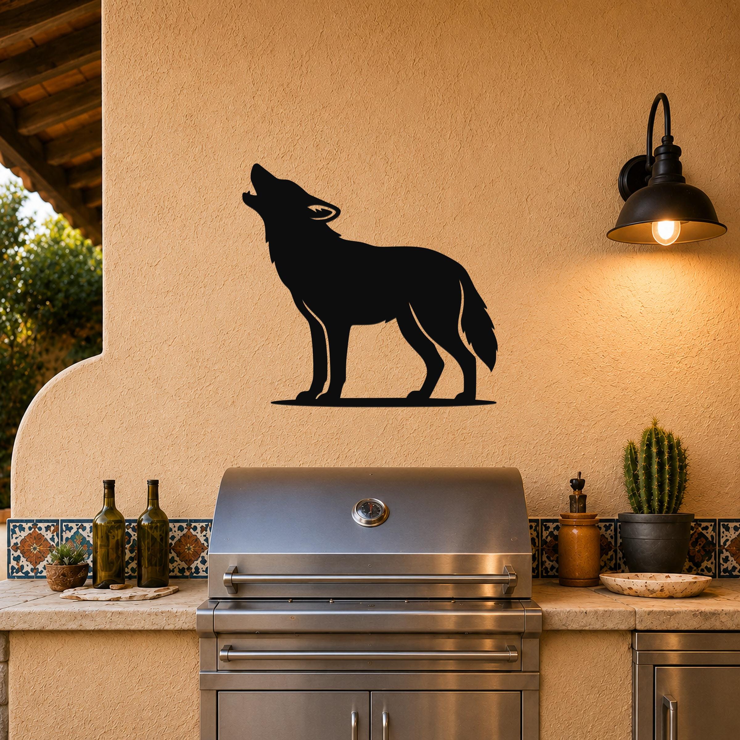 Black metal coyote wall art in a howling silhouette, mounted on a stucco wall above a stainless steel grill in an outdoor kitchen.