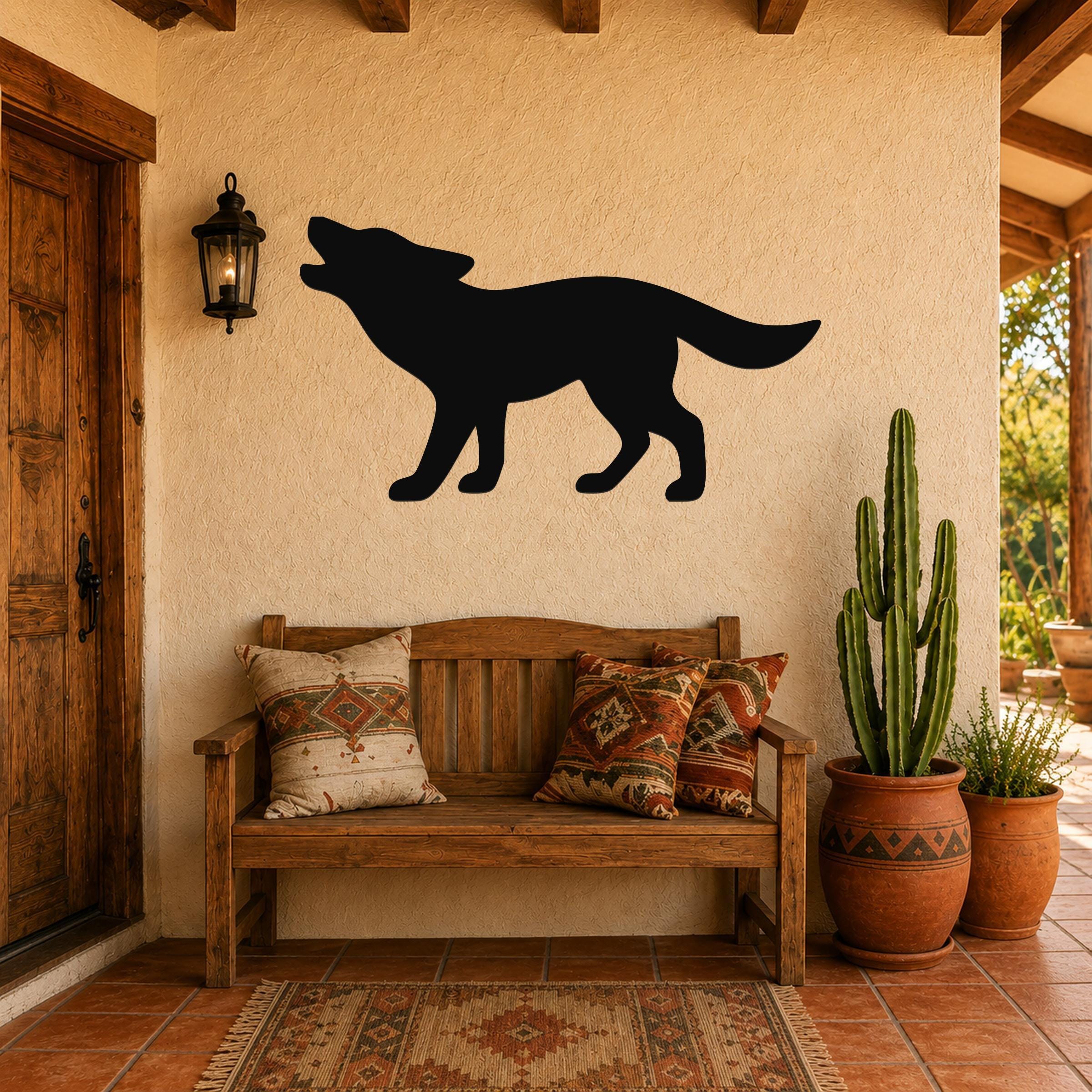 Black metal coyote wall art in a howling silhouette, mounted on a stucco wall above a wooden bench in a rustic patio entryway.