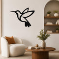 Black metal hummingbird wall art with a silhouette design, mounted on a living room wall above a white armchair.