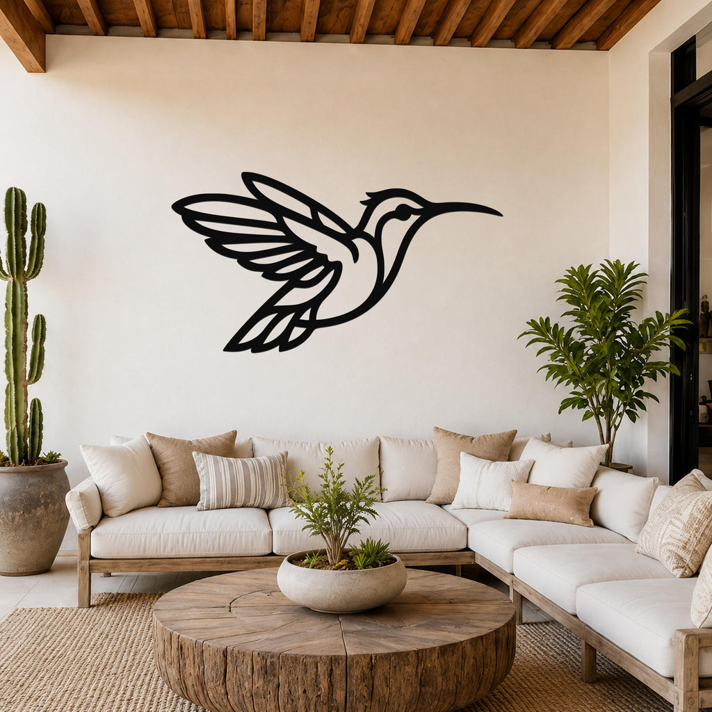 Black metal hummingbird wall art with wing and tail cutouts, mounted above a white sofa in a living room with wooden beams and plants.