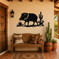 Black metal wall art silhouette of a javelina with cacti, mounted on a stucco wall above a wooden bench in a rustic patio entry.