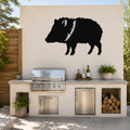 Black metal javelina wall art silhouette with white detail on the neck, mounted on an outdoor kitchen wall above a stainless steel grill.
