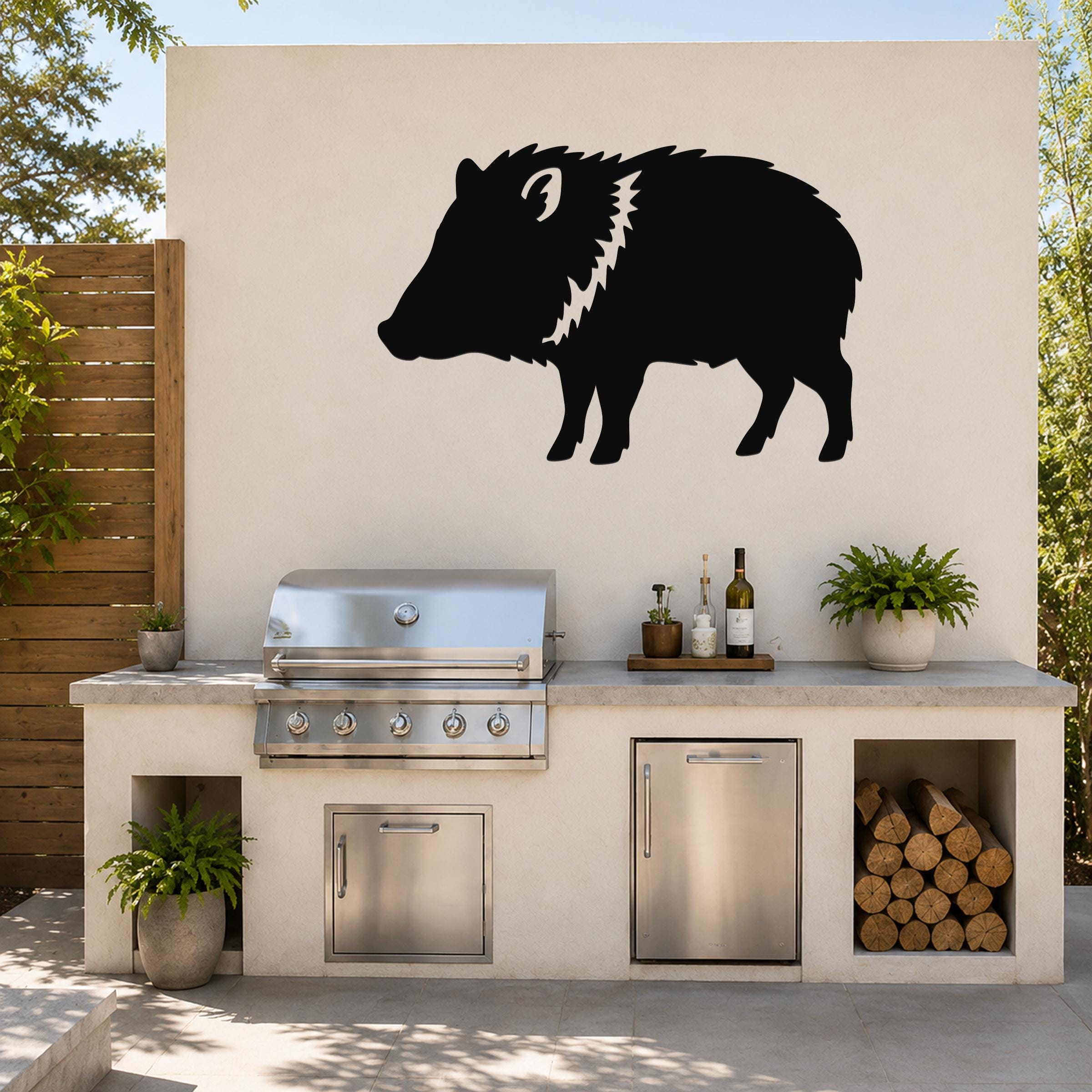 Black metal javelina wall art silhouette with white detail on the neck, mounted on an outdoor kitchen wall above a stainless steel grill.