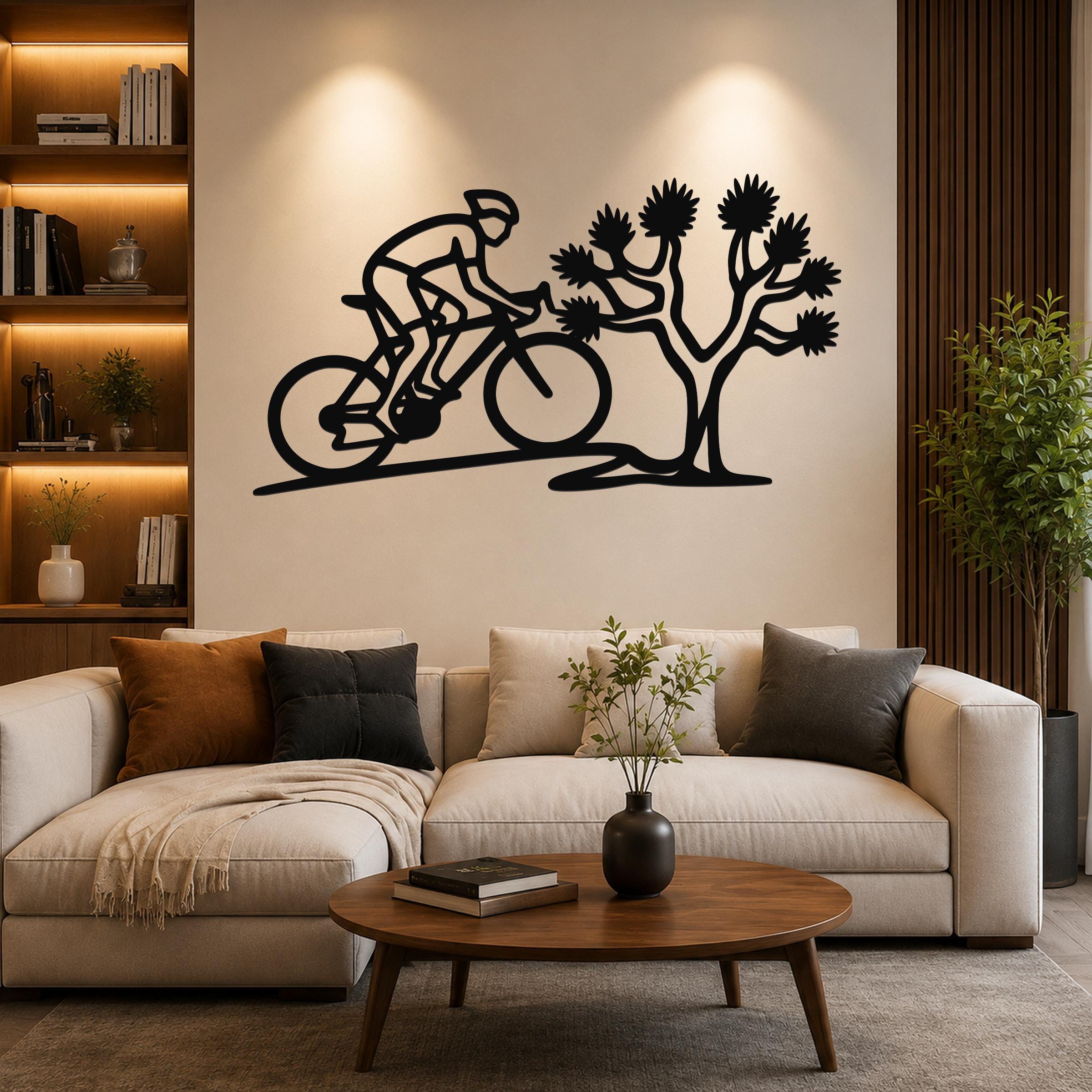 Black metal wall art cutout of a cyclist on a mountain bike next to a Joshua tree, mounted above a beige sofa in a living room.