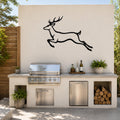 Black metal jumping deer wall art silhouette mounted on an outdoor kitchen wall above a stainless steel grill and counter.