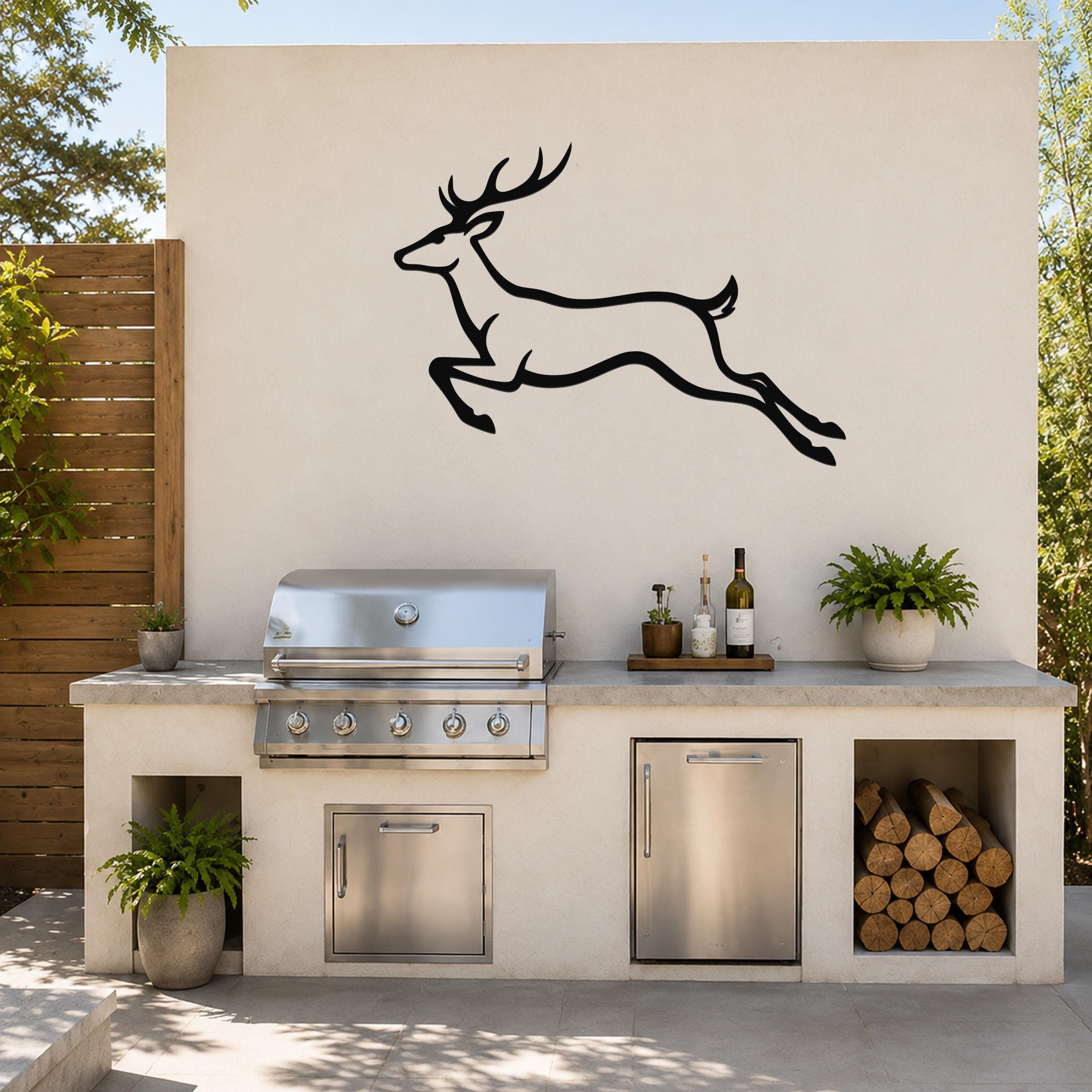 Black metal jumping deer wall art silhouette mounted on an outdoor kitchen wall above a stainless steel grill and counter.