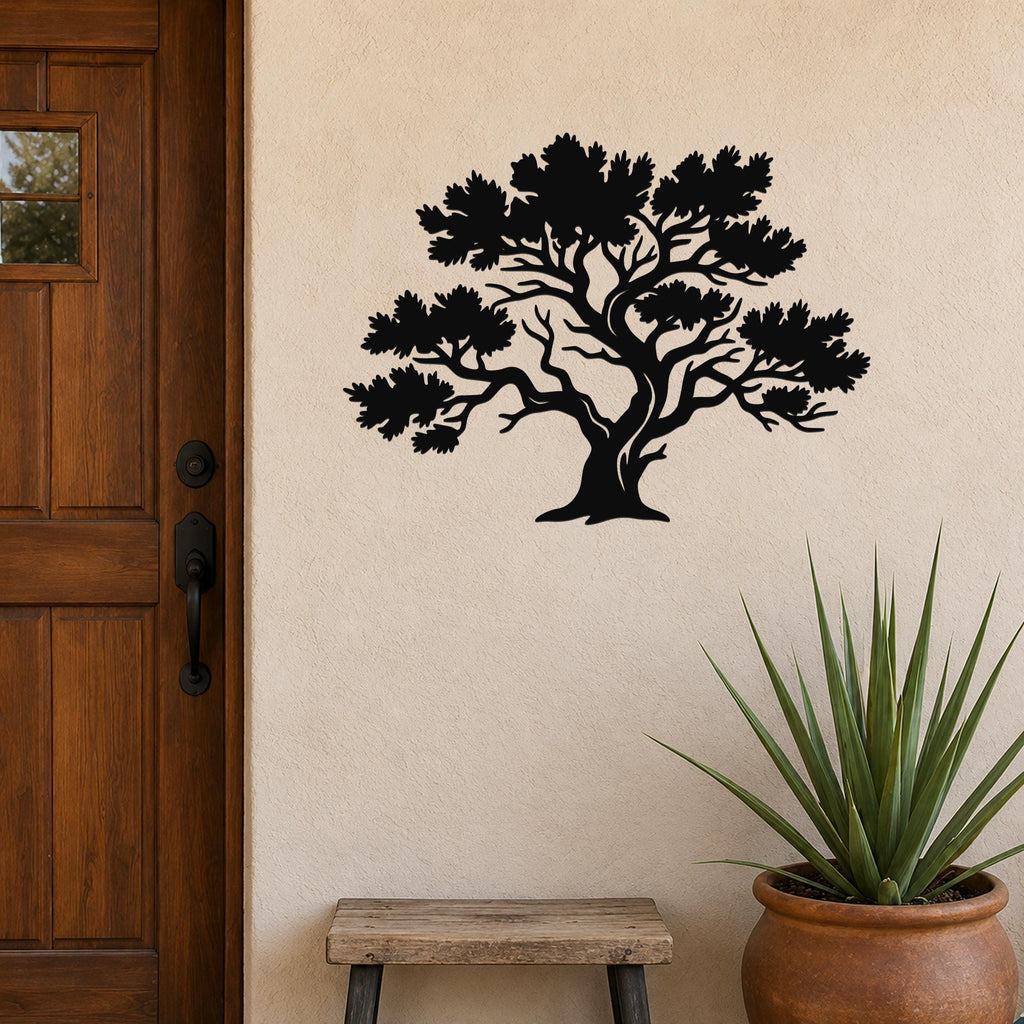 Black metal juniper tree wall art with detailed branch and leaf cutouts, mounted on a beige exterior wall beside a wooden door and a potted plant.