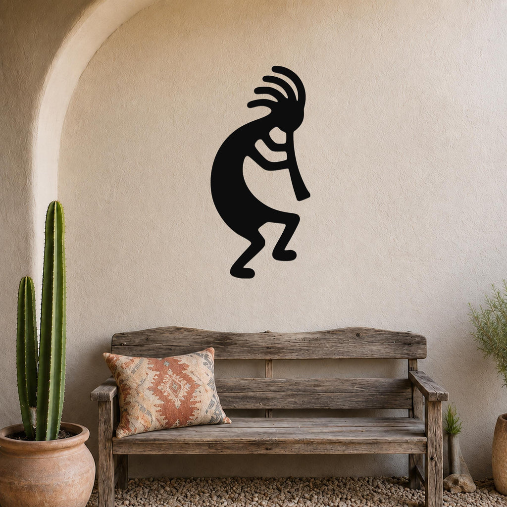 Black metal Kokopelli wall art silhouette with flute and feathered headdress, mounted on a stucco wall above a wooden bench in a patio setting.