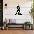 Black metal lighthouse wall art with a silhouette design, mounted on a white shiplap wall above a wooden bench on a porch.
