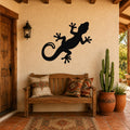 Black metal lizard wall art silhouette mounted on a stucco wall above a wooden bench in a patio entryway.