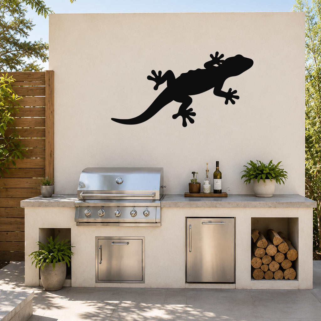 Black metal lizard wall art silhouette mounted on a light-colored outdoor wall above a stainless steel grill and countertop.