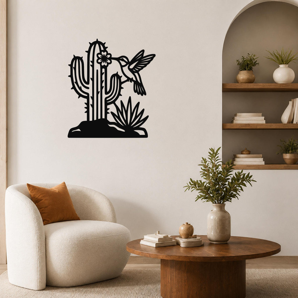 Black metal wall art featuring a cactus, flower, and hummingbird cutout, mounted on a living room wall above a white armchair.