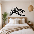 Black metal wall art silhouette of a snowboarder in motion, mounted above a wooden bed in a bedroom.