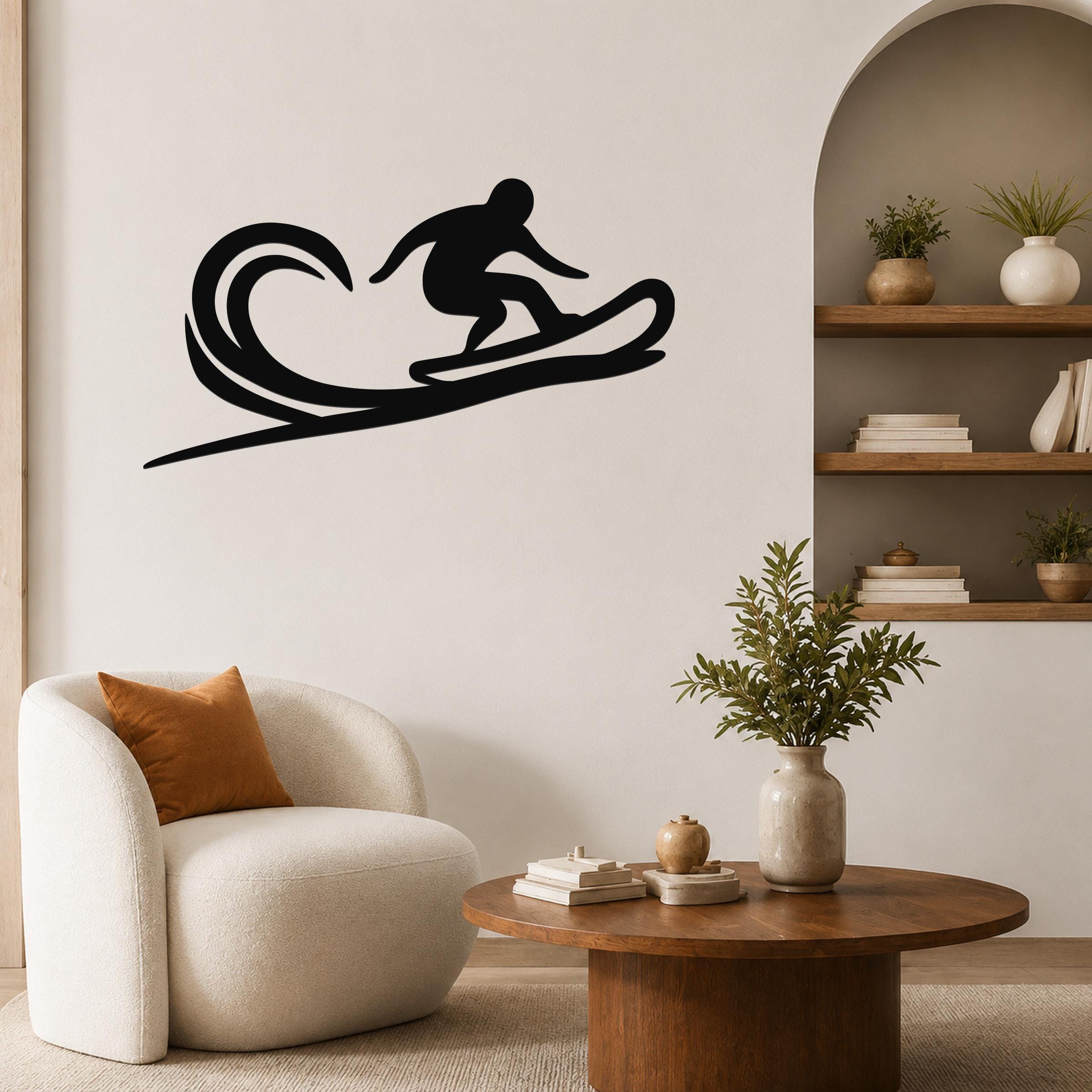 Black metal wall art silhouette of a surfer riding a wave, mounted on a living room wall above a white armchair.