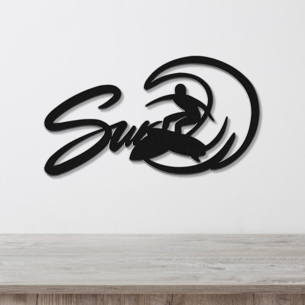 Black metal wall art featuring a surfer silhouette riding a wave, with the word "Surf" in cursive script, mounted on a white wall above a light wood surface.