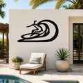 Black metal surfer wall sculpture with wave cutout, mounted on a white outdoor wall above a lounge chair near a pool.