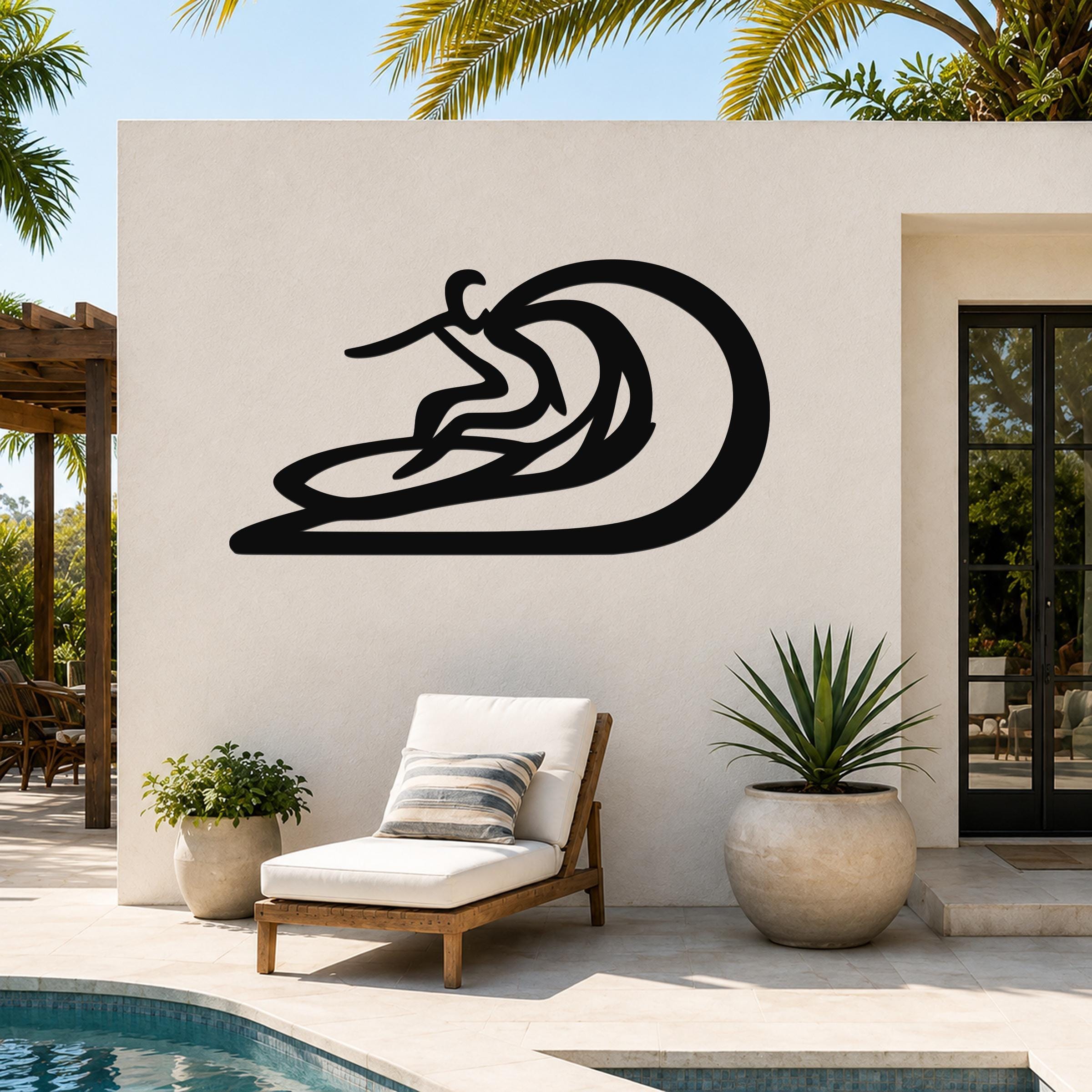 Black metal surfer wall sculpture with wave cutout, mounted on a white outdoor wall above a lounge chair near a pool.