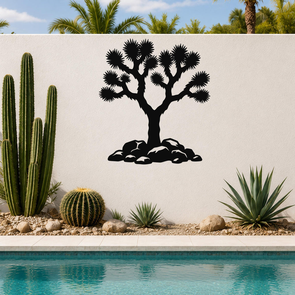 Black metal wall art silhouette of a Joshua tree with spiky branches and rocks at its base, mounted on a white outdoor wall above a poolside garden.