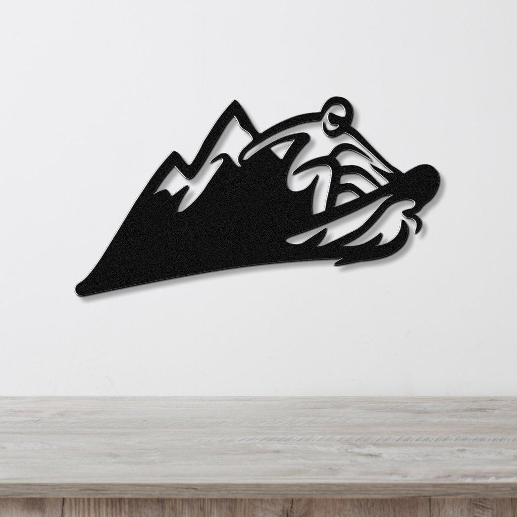 Black metal wall art featuring a bold snowboarder silhouette cutout over mountain peaks, mounted on a white wall above a light wood counter.