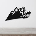 Black metal wall art featuring a bold snowboarder silhouette cutout over mountain peaks, mounted on a white wall above a light wood counter.