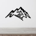Black metal wall art featuring a snowboarder silhouette within a mountain range cutout, mounted on a white wall above a light wood counter.