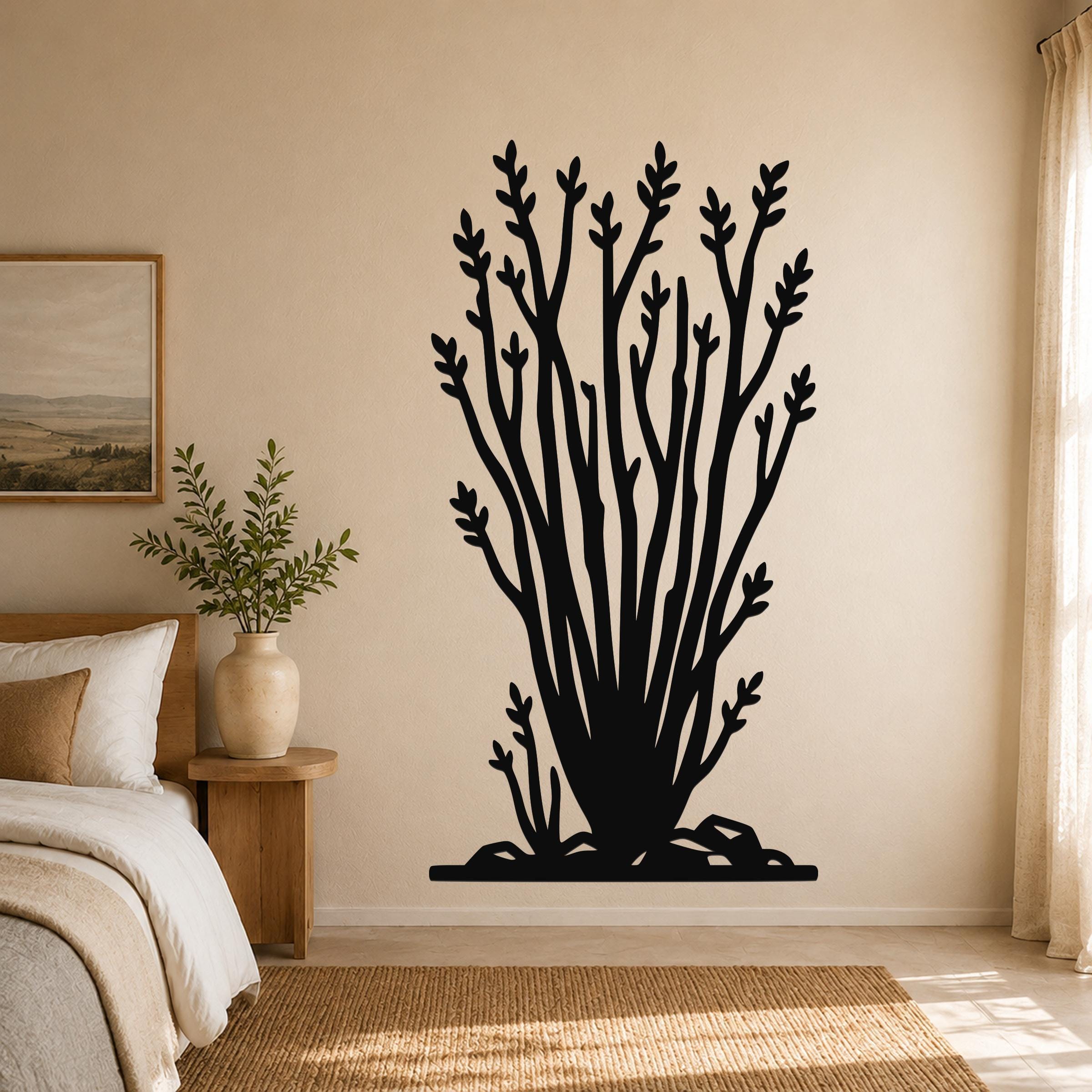 Black metal ocotillo wall art with branching cutouts, mounted on a beige bedroom wall above a bed.
