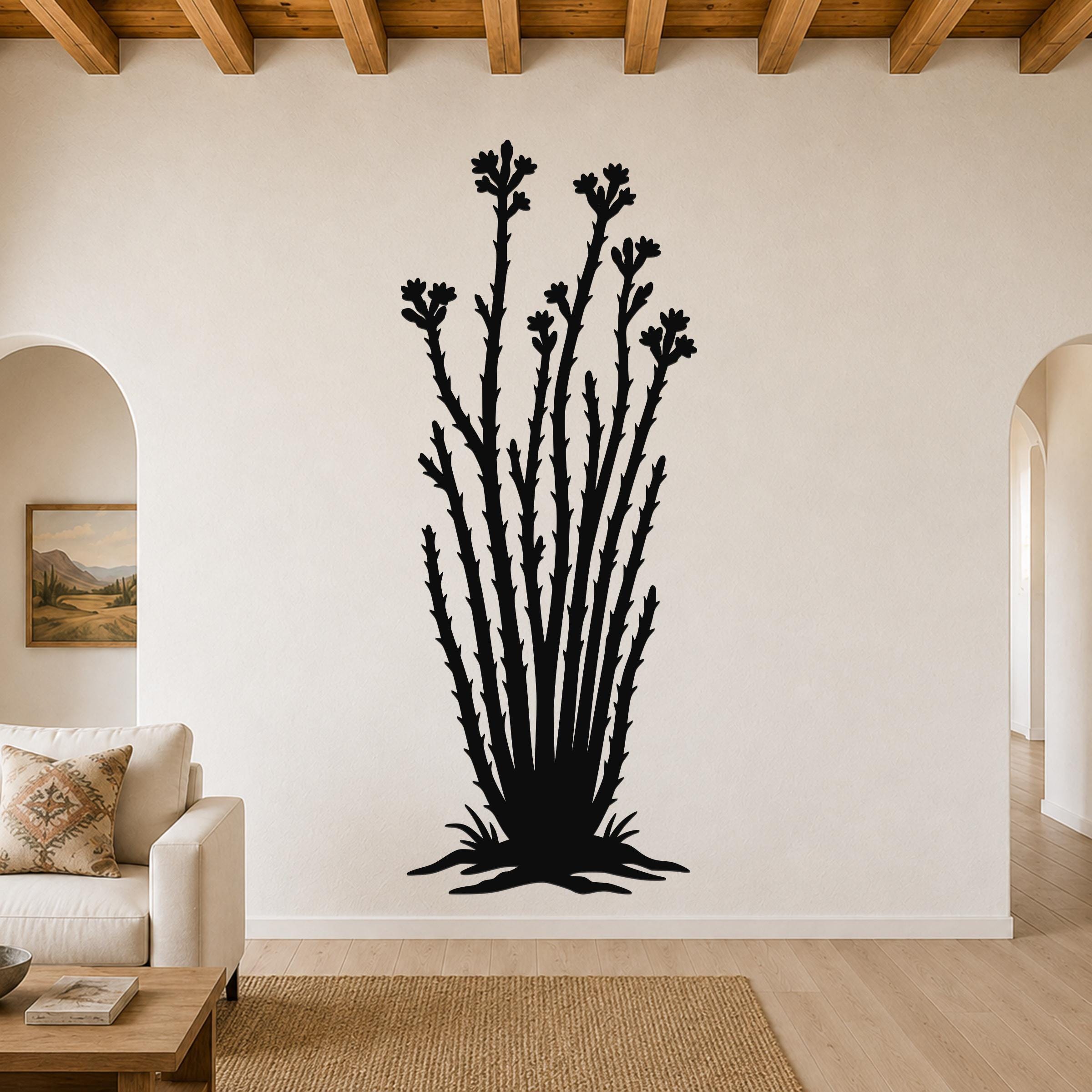 Black metal ocotillo wall art with flower and branch cutouts, mounted on a living room wall above a sofa.
