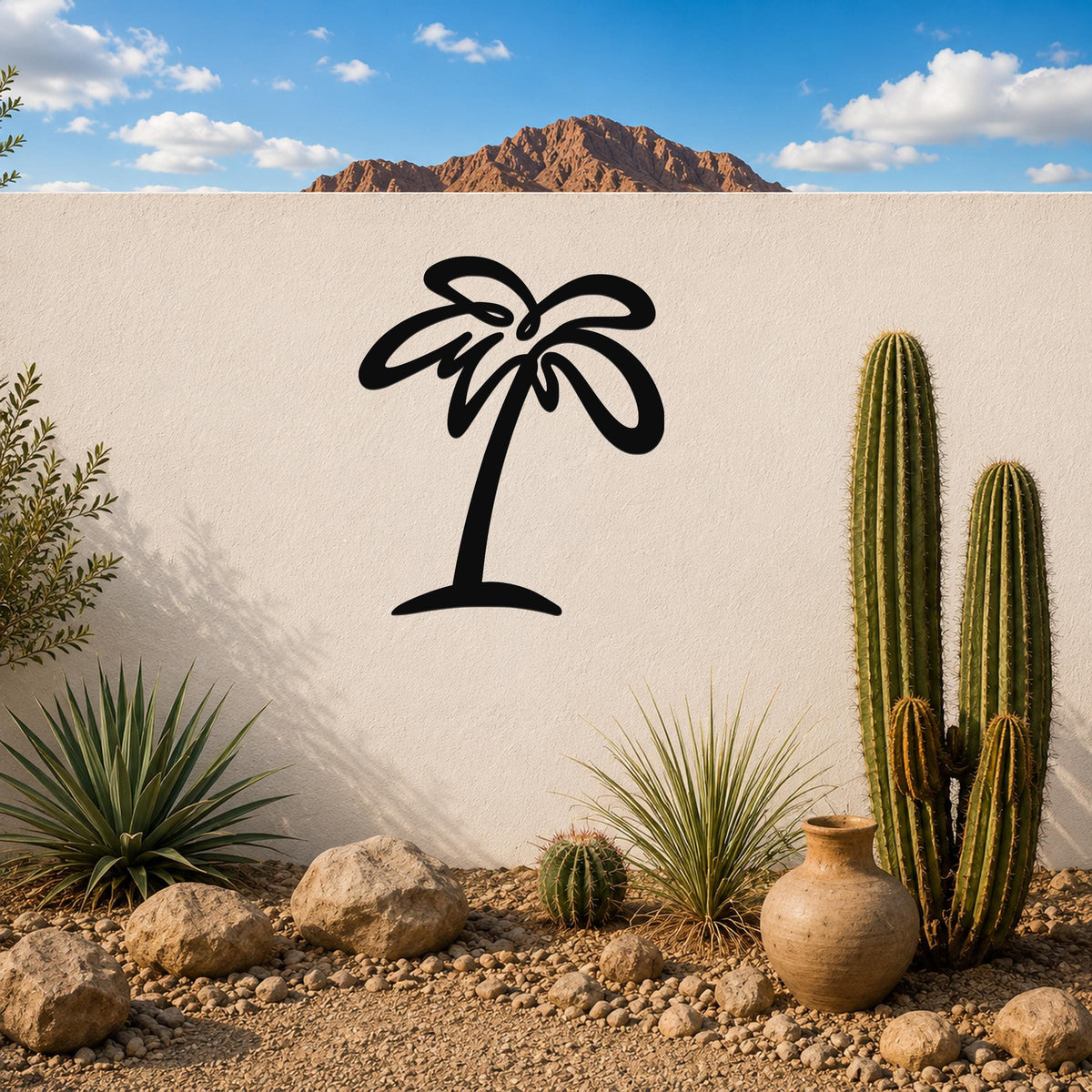 Black metal palm tree wall art with flowing frond cutouts, mounted on a white outdoor wall above a desert garden with cacti and rocks.