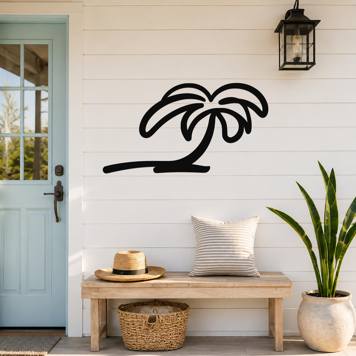 Black metal palm tree wall art with flowing frond cutouts, mounted on a white shiplap wall above a wooden bench in a coastal entryway.
