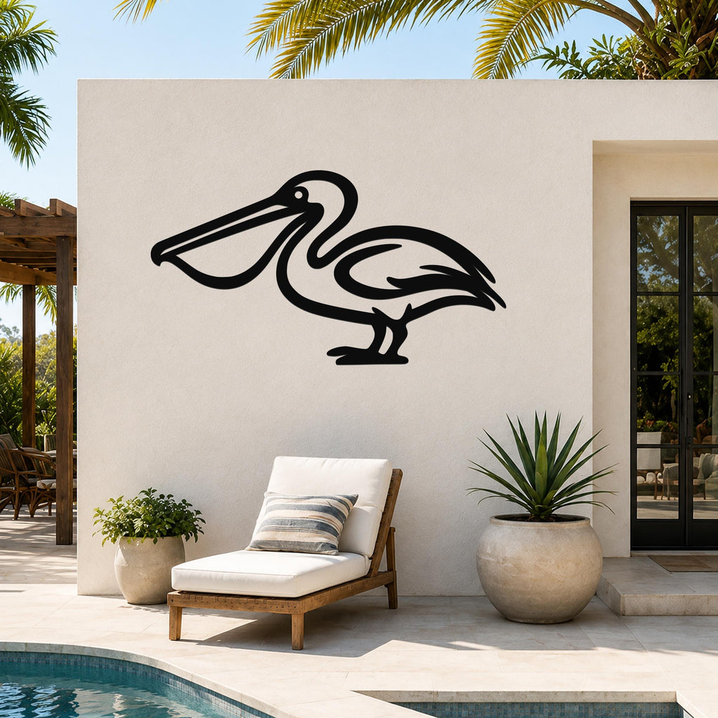 Black metal pelican wall art silhouette mounted on an outdoor patio wall above a lounge chair, with palm trees and a pool in the background.