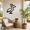 Black metal pelican wall art silhouette mounted on a light-colored wall above a wicker chair in a coastal patio setting.