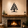Black metal pine tree wall art with layered silhouette cutouts, mounted above a stone fireplace in a rustic living room.