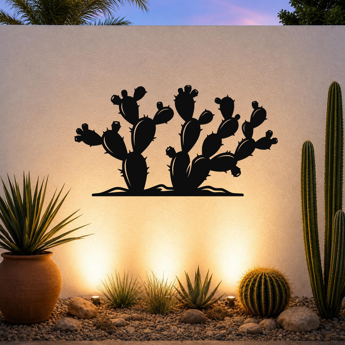 Black metal wall art in the silhouette of a prickly pear cactus with multiple pads and spines, mounted on a light-colored outdoor wall above a desert garden with potted plants and ground lights.