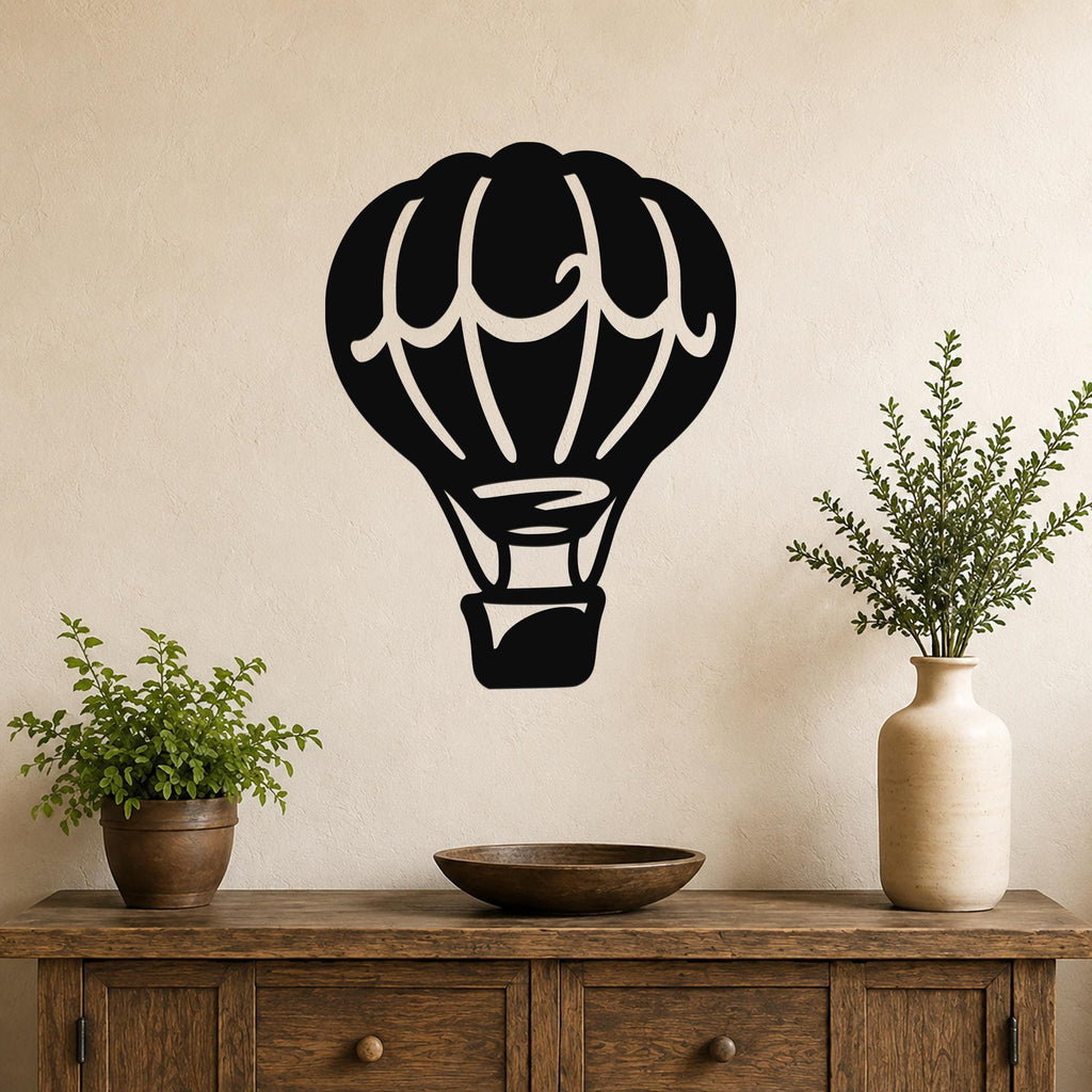 Black metal hot air balloon wall art with internal cutout details, mounted on a beige wall above a wooden console table with potted plants.