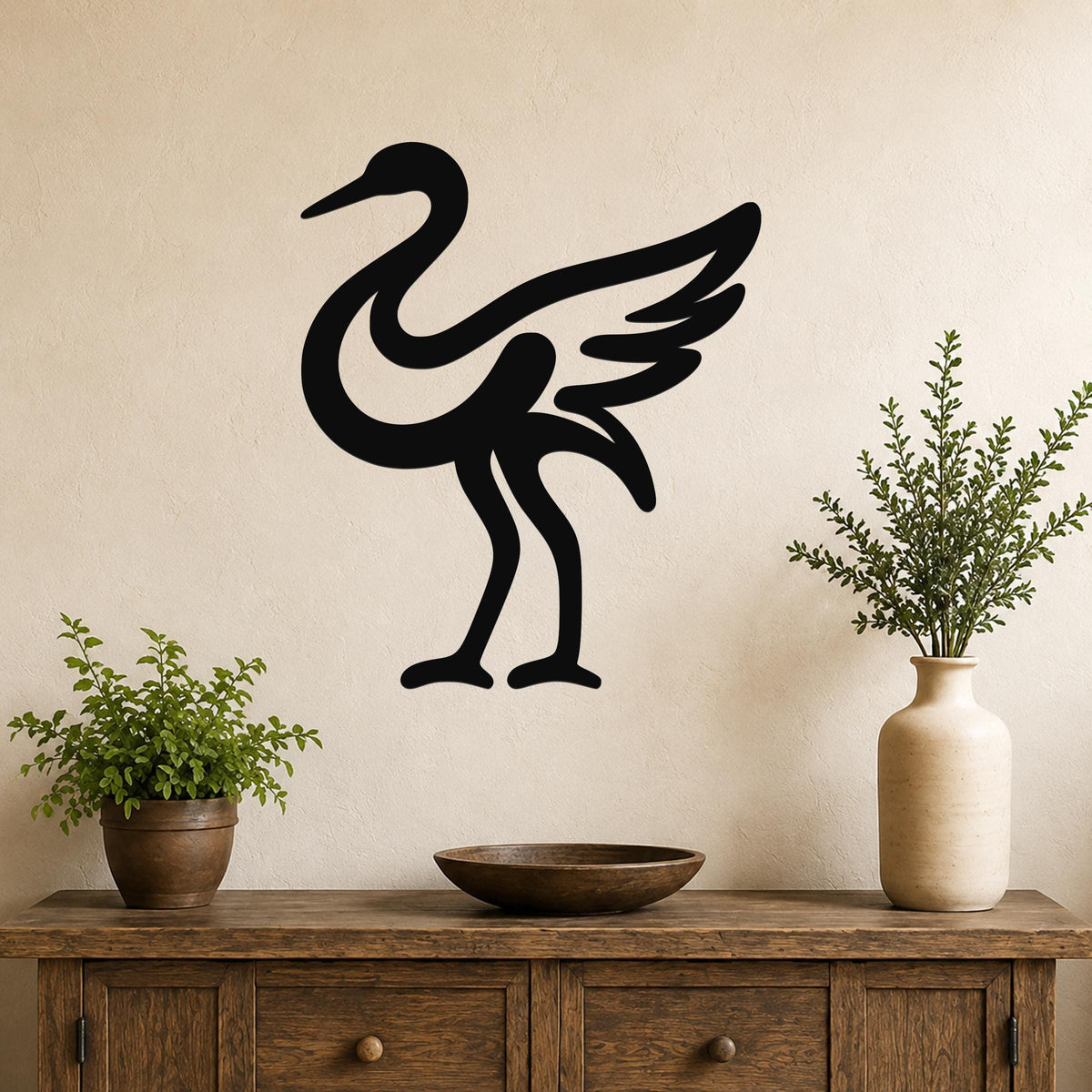 Black metal crane wall art with a minimalist silhouette design, mounted on a beige wall above a wooden console table with potted plants.