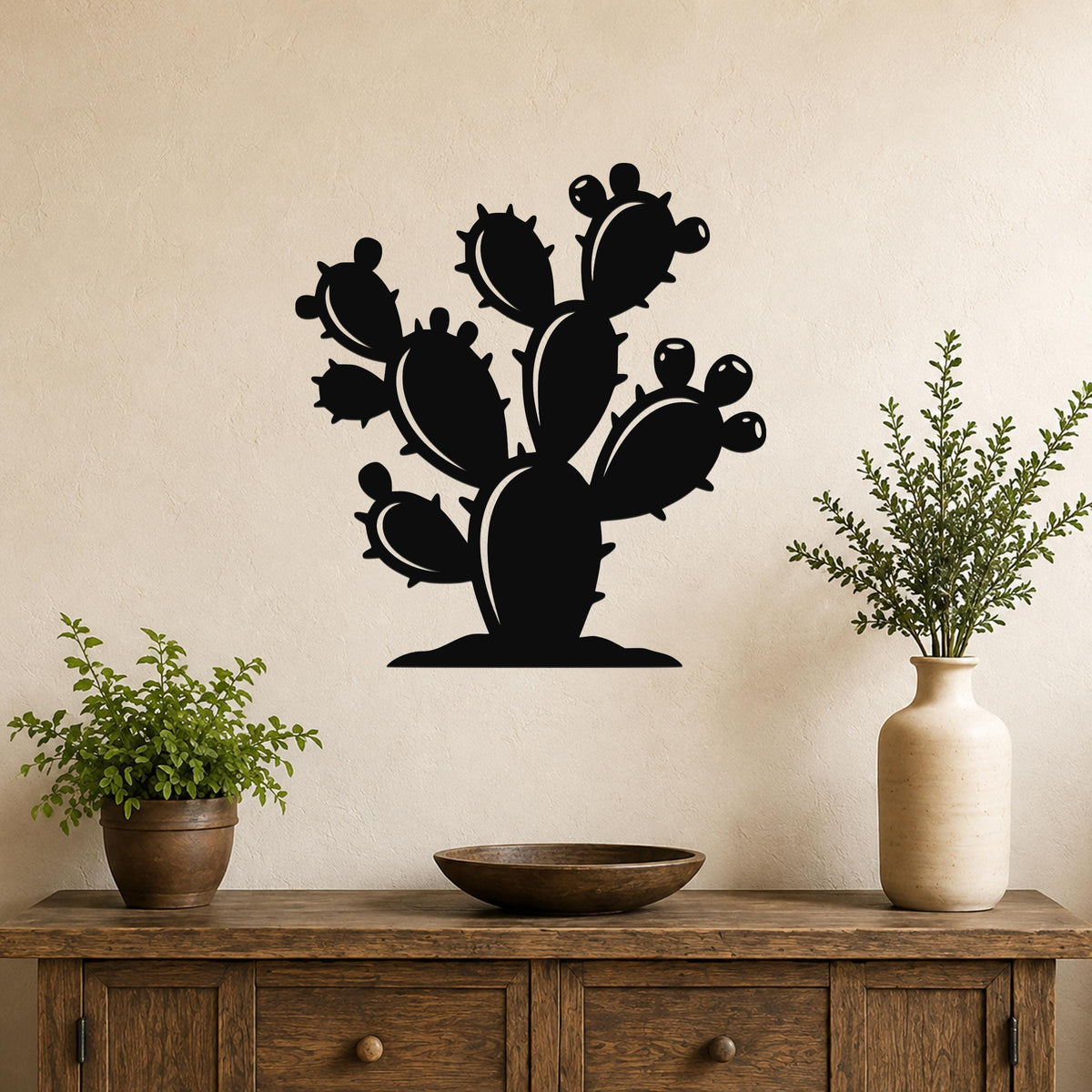 Black metal prickly pear cactus wall art with detailed paddle and spine cutouts, mounted on a beige wall above a wooden console table with potted plants.