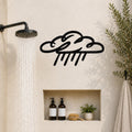 Black metal rain cloud wall art with raindrop cutouts, mounted on a bathroom wall above a built-in shelf.
