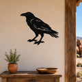 Black metal raven wall art silhouette with detailed feather cutouts, mounted on a beige wall above a wooden table in a rustic outdoor entryway.